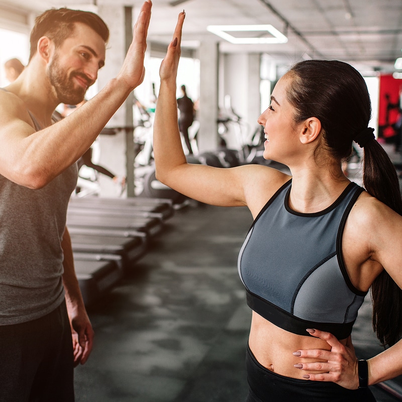 Un homme et une femme souriants se donnent un high-five dans une salle de sport, célébrant un succès après un entraînement de fitness.
