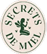 Logo rond Secrets de Miel en vert foncé et beige. Une fée ailée délicate est assise, tenant une fleur, symbolisant la nature et le miel.