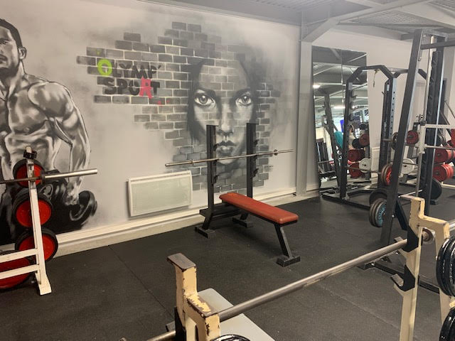 Mural d'un homme musclé et d'une femme dans une salle de sport, avec texte "OLYMP SPORT", équipements de musculation et un banc.